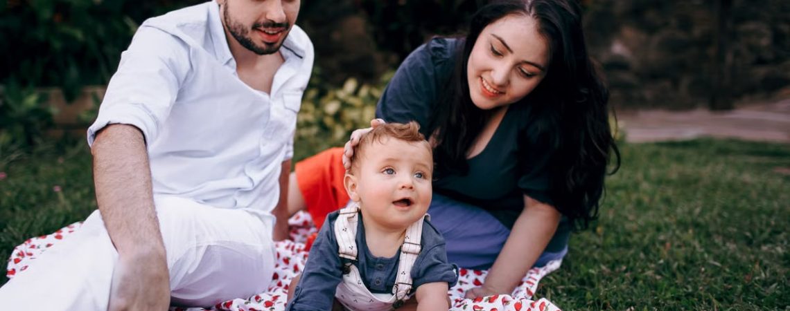 A joyful family enjoying a picnic outdoors during summer. Smiling parents with their baby on a blanket.