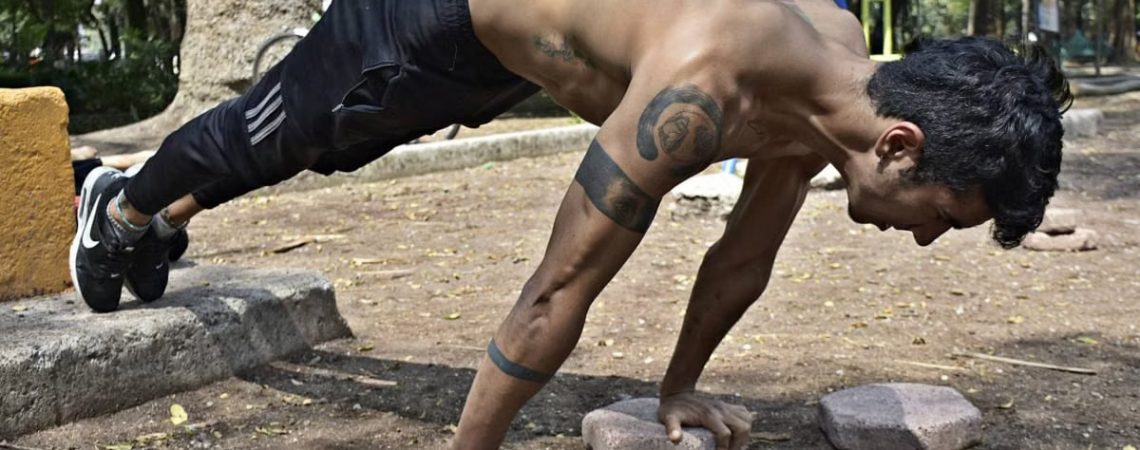 Athletic man performing elevated push-ups on rocks in a park setting.